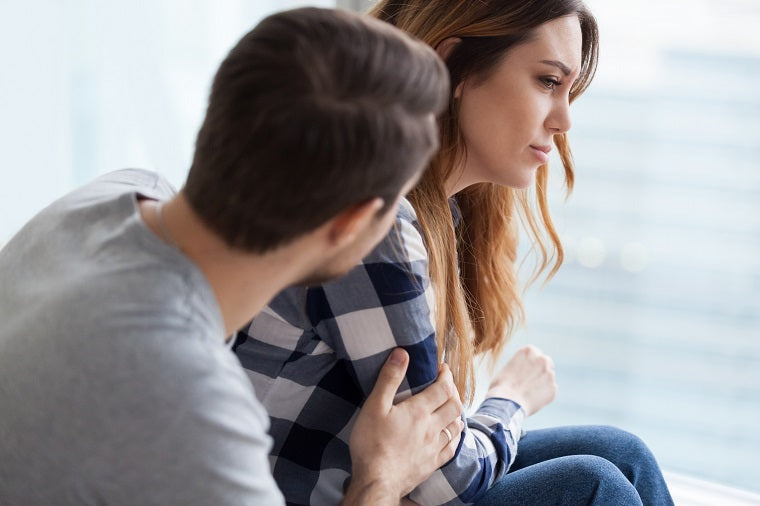 A man in his 30s with short brown hair and a gray shirt comforts a woman with long blonde hair who appears very upset. 