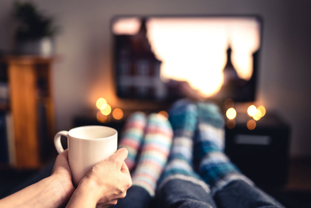 Couple snuggling up in the living room, drinking a hot chocolate while watching their favorite move