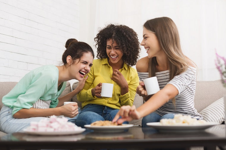 A group of young women joyfully drink coffee and laugh hard. 