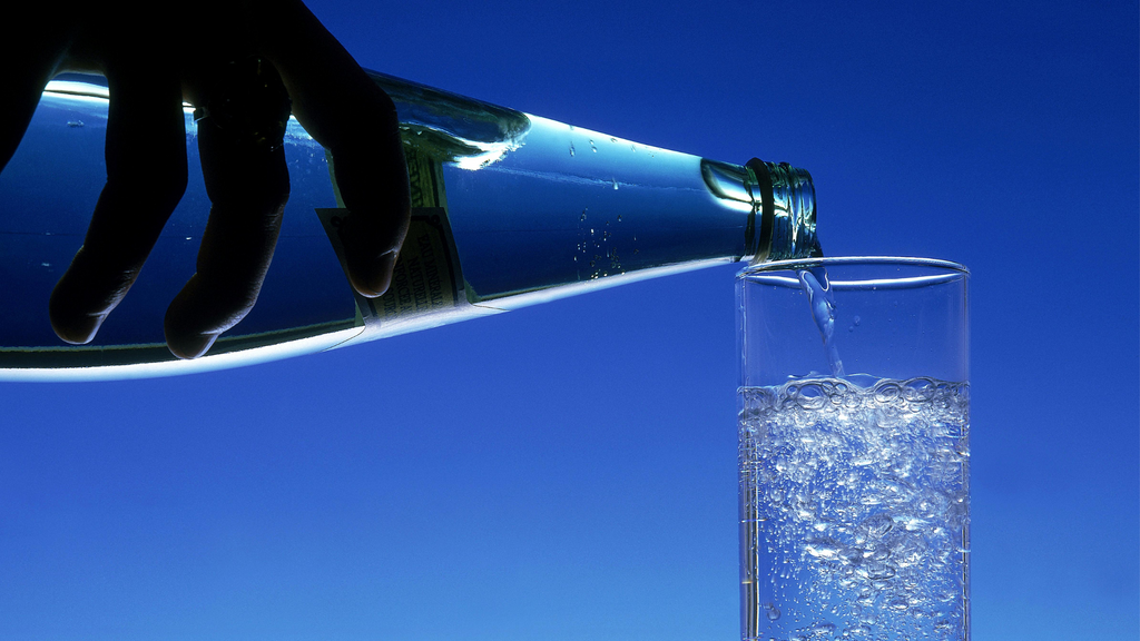 Glass bottle of sparkling water being poured into a glass cup