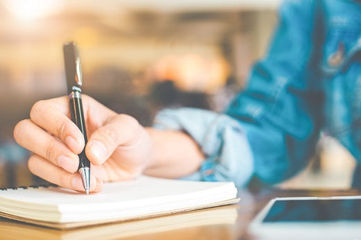 a woman writes into her migraine journal with a pen. 