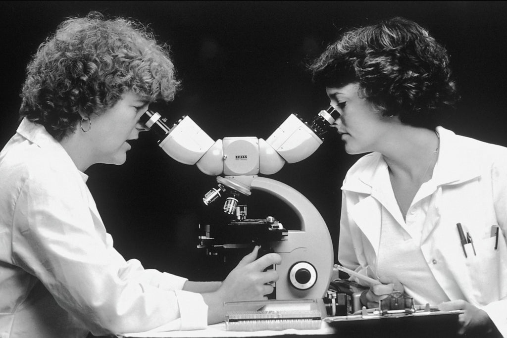 Female med techs peer through a microscope. 