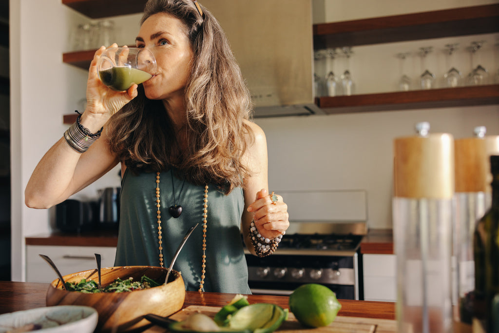 A woman is drinking a green smoothie in her kitchen 